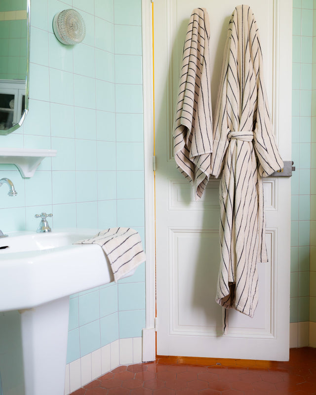 Bademantel NARAM Creme & Ink und ein Handtuch in derselben Farbe hängen an einer Badezimmertür