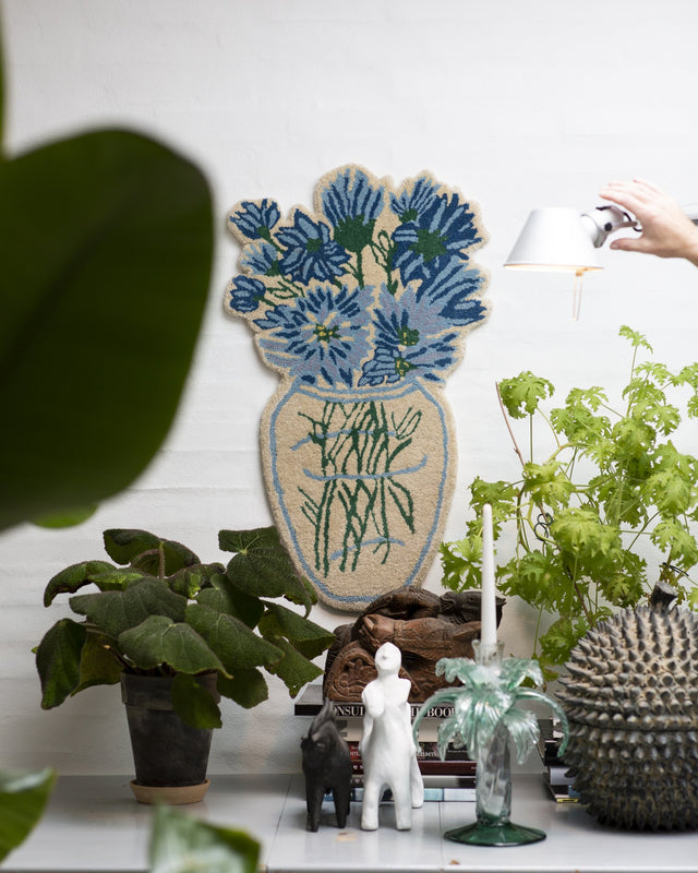 Blumenvasen-Teppich Blue Daisy an der Wand über einem Tisch mit Pflanzen, Kerzenhalter und Figuren