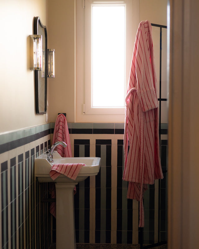 Badezimmer mit gestreiften Fliesen, Handtüchern und Bademantel NARAM in Rosa mit roten Streifen