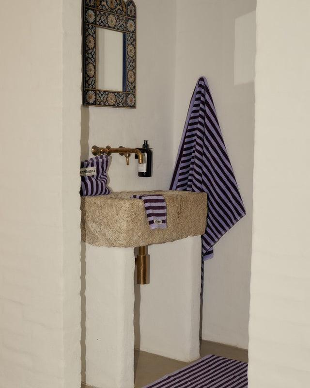 Badezimmer mit Steinwaschbecken, hängendem Duschtuch und Waschlappen in Weinrot und Lavendelblau