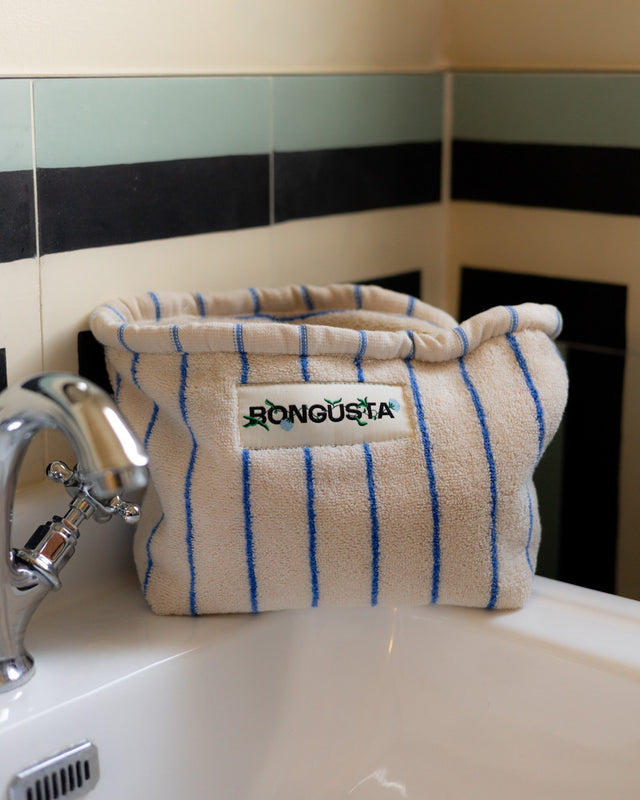 Kulturbeutel NARAM in Moonbeam & Ultramarine auf dem Rand einer Badewanne neben dem Wasserhahn