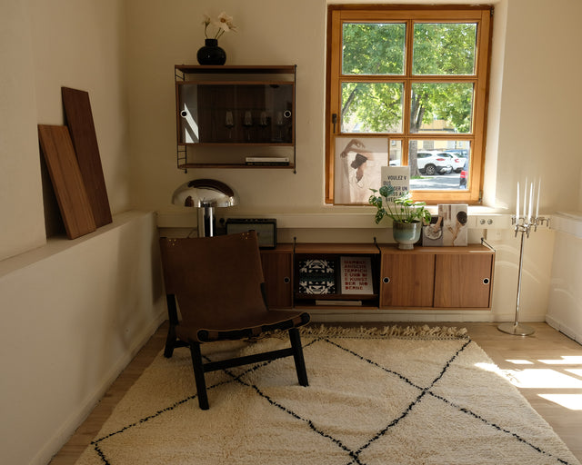 Beni Ourain CLASSIC ONE mit braunem Ledersessel vor Sideboard und Fenster