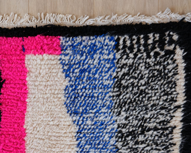 Teppichende mit Streifen in Neonpink, Blau und Schwarz-Weiß, dunkler Kante und hellen Fransen