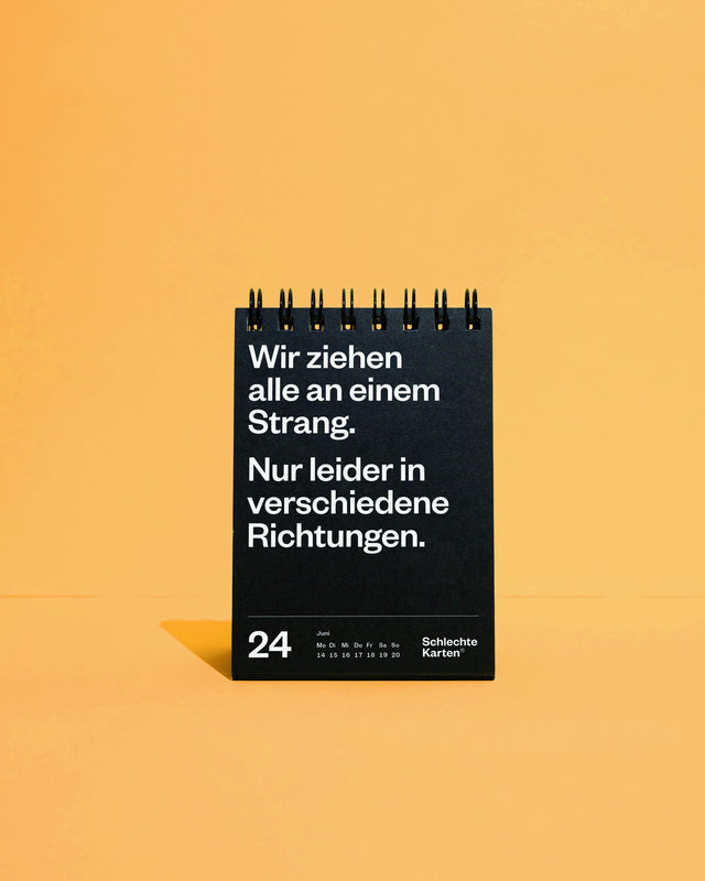 Tischkalender vor orangefarbenem Hintergrund, aufgeschlagen beim 24. Juni mit dem Spruch über den Strang in verschiedene Richtungen.