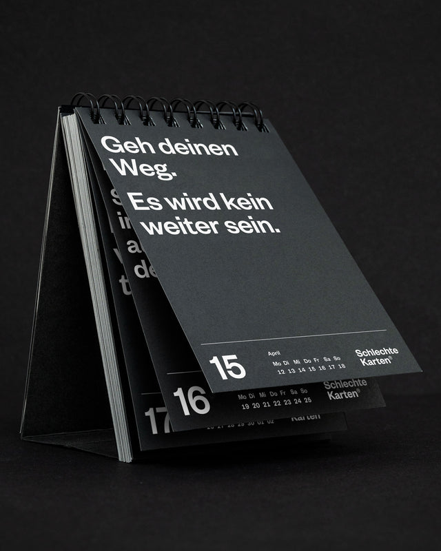 Tischkalender schräg von vorn auf schwarzem Grund, der Rückdeckel steht als Aufsteller nach hinten ab.