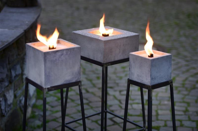 Nahaufnahme: Alle drei eckigen Betonfeuer auf Ständern mit entzündeter Flamme.