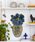 Teppich Blue Daisy an einer weißen Wand zwischen Regalbrettern mit Keramikkugeln, Pflanze und Korb