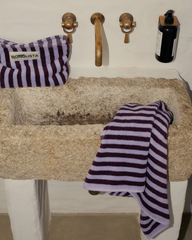 Handtuch in Weinrot und Lavendelblau über dem Rand eines Waschbeckens aus Stein, Messingarmaturen
