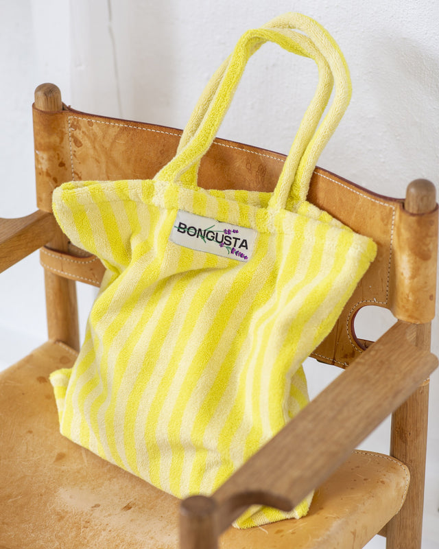 Gelb-weiß gestreifte Tote Bag aus Frottee steht auf einem Holzstuhl mit Lederbespannung