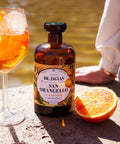 Orangello Spritz im Weinglas mit Eiswürfeln und Orangenscheibe neben der Flasche San Orangello und einer halben Orange