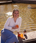 Frau in weißer Bluse sitzt mit einem Glas San Orangello am Brunnenrand, neben ihr Flasche und Orangen