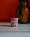 Kaffeebecher POP ART in bubble, rosa mit dunklen Wellenlinien, vor roter Wand neben einem alten Steingutkrug