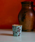 Kaffeebecher SURREAL in patina, vor roter Wand neben einem alten Steingutkrug