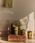 Teakholz-Sockel mit gestapelten Bechern aus der Reihe 70s Ceramics vor einer gefliesten Wand
