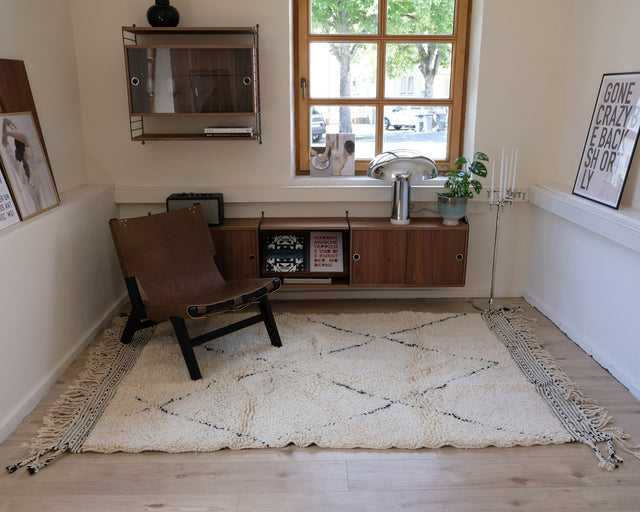 Blick in den Raum mit Fenster und Sideboard, der Teppich füllt den Bereich vor dem Sessel aus.