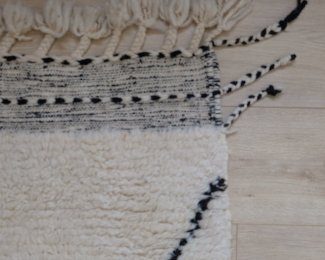 Detail: Kelimrand mit schwarz-weißem Muster und zweifarbigen Kordeln an der Ecke