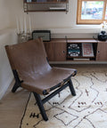 Wollweißer Berberteppich mit braunen Linien und Zeichen unter einem Ledersessel, dahinter ein Sideboard aus Holz