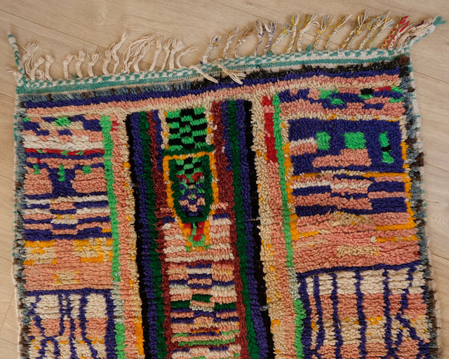 Schmalseite mit grün-schwarzem Mittelstreifen, blauen Feldern und bunten Fransen