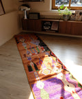 Langer bunter Läufer in Orange und Lila vor einem Sideboard aus Holz, im Sonnenlicht
