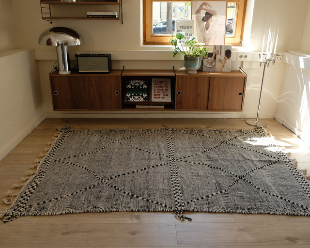 Zanafi-Teppich 1,45 x 2,20 m im Raum: grau gesprenkelter Grund, gepunktete Rauten und ein kariertes Band in der Mitte