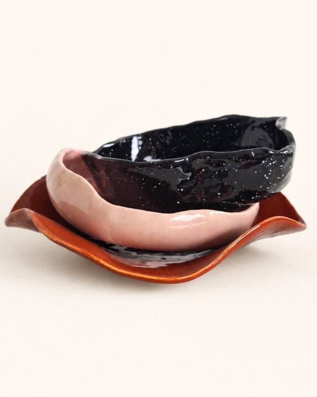 Eine rosa und eine schwarz gesprenkelte Keramik-Bowl auf einer welligen, rotbraun glasierten Platte.