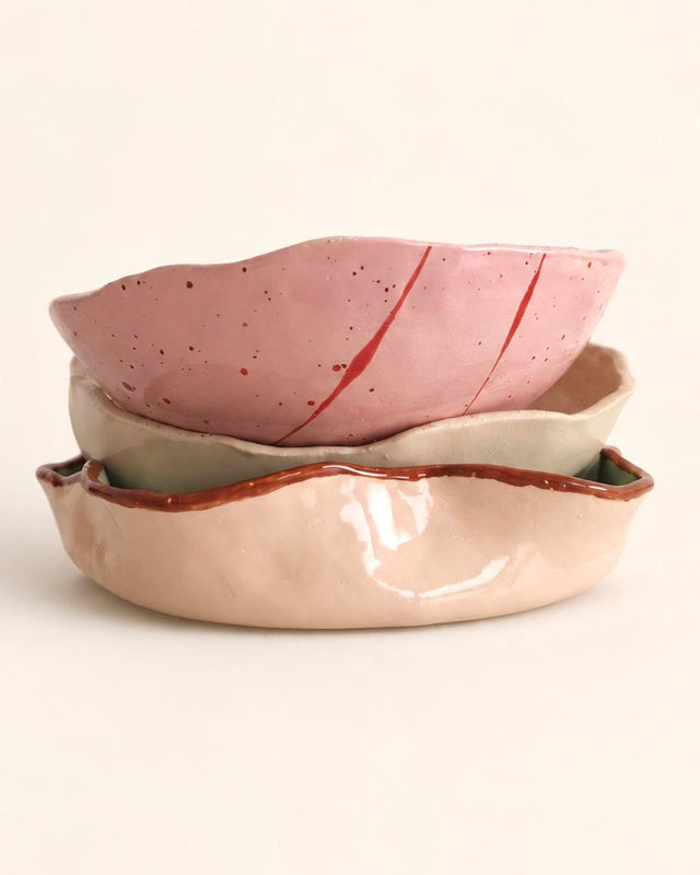 Drei gestapelte, wellige Keramikschalen in Rosa mit roten Streifen, Creme und Apricot.