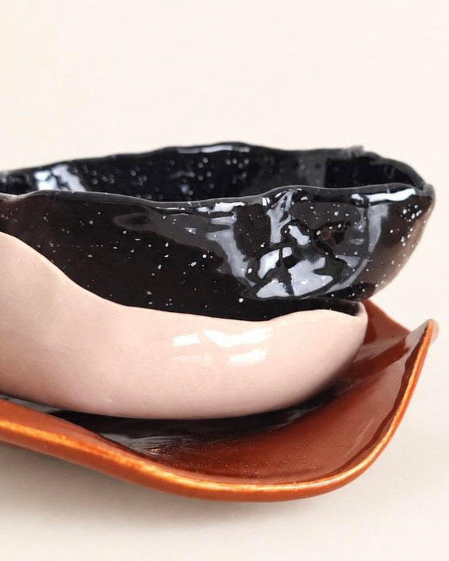 Nahaufnahme der glänzenden Glasuren: schwarz gesprenkelte Bowl über rosa Schale und rotbrauner Platte.