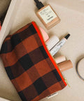 Geöffnete Kosmetiktasche SOFIA in Big Vichy Ginger auf einem Tablett mit Foundation, Lippenstift und Concealer