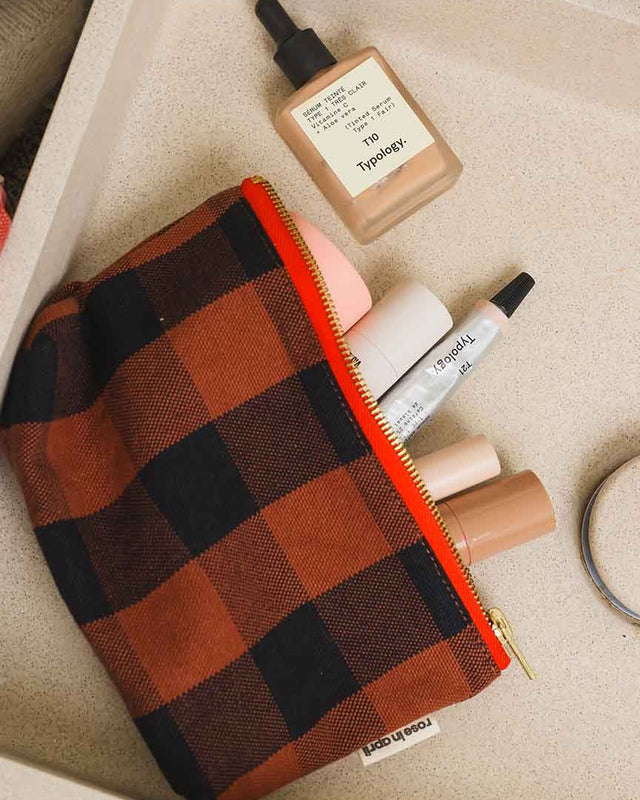Geöffnete Kosmetiktasche SOFIA in Big Vichy Ginger auf einem Tablett mit Foundation, Lippenstift und Concealer