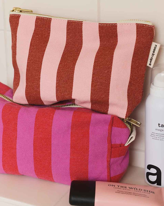 Kulturbeutel DESI in Pink und Tomatenrot im Bad, darauf ein rosa-rot gestreiftes Täschchen