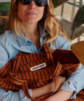 Frau im Jeanshemd mit Sonnenbrille hält die Tote Bag ELISABETH in Ginger Tennis Stripes im Arm