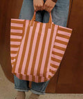 Tote Bag ELISABETH in Strawberry/Caramel Stripes, an beiden Henkeln vor einer Jeans gehalten