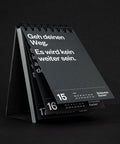 Tischkalender schräg von vorn auf schwarzem Grund, der Rückdeckel steht als Aufsteller nach hinten ab.