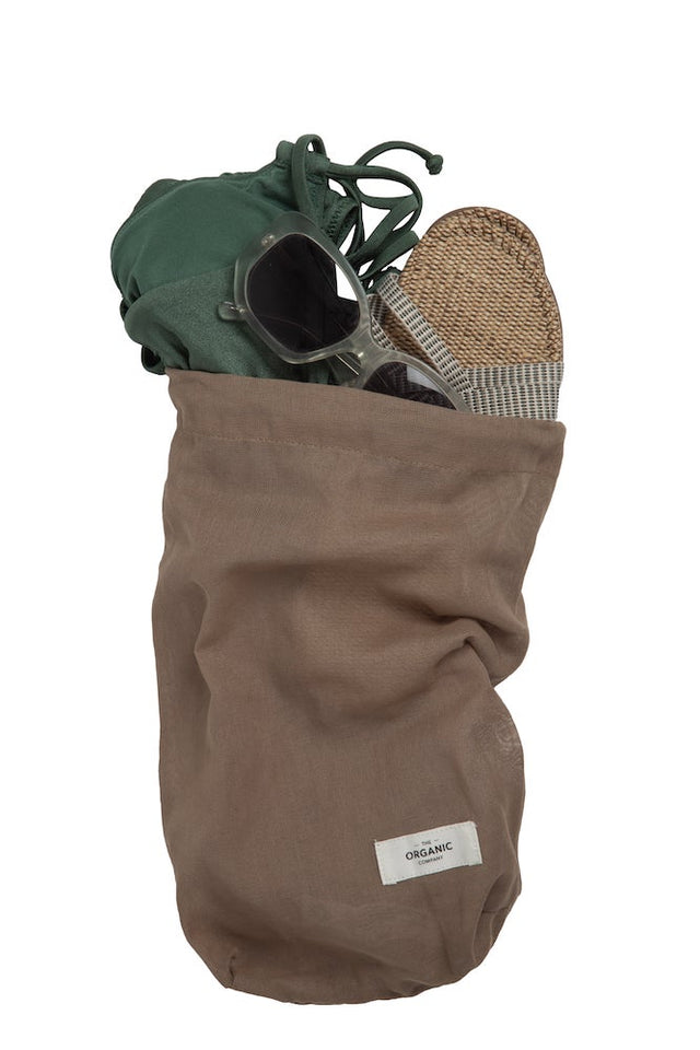 Mittelgroßer Stoffbeutel aus Bio-Baumwolle in der Farbe Clay, gefüllt mit Badesachen, Sonnenbrille, Sandalen.