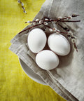 Leinenserviette in Natur mit Eiern und Palmzweig auf gelber Tischdecke.