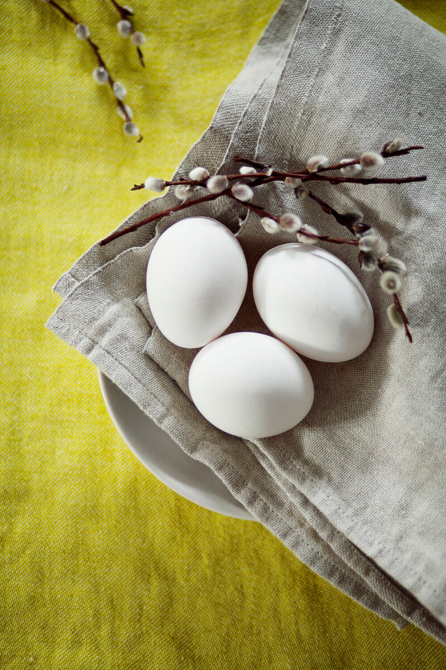Leinenserviette in Natur mit Eiern und Palmzweig auf gelber Tischdecke.